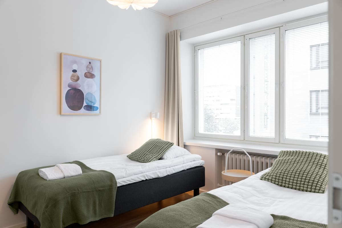 A hotel room with two beds, a window with blinds, a radiator, and a painting on the wall.