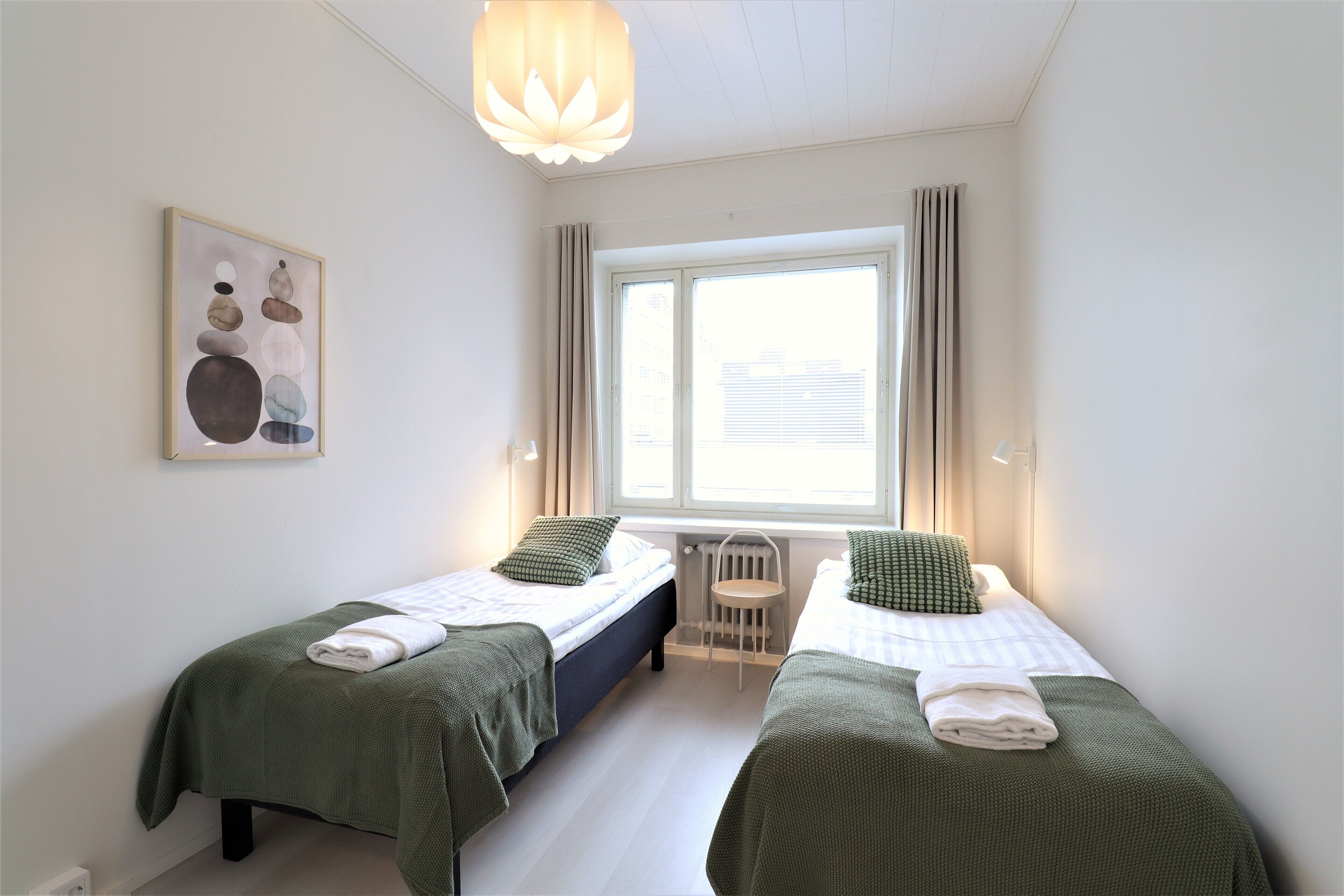 A room with two beds, a window, a radiator, and a painting on the wall.