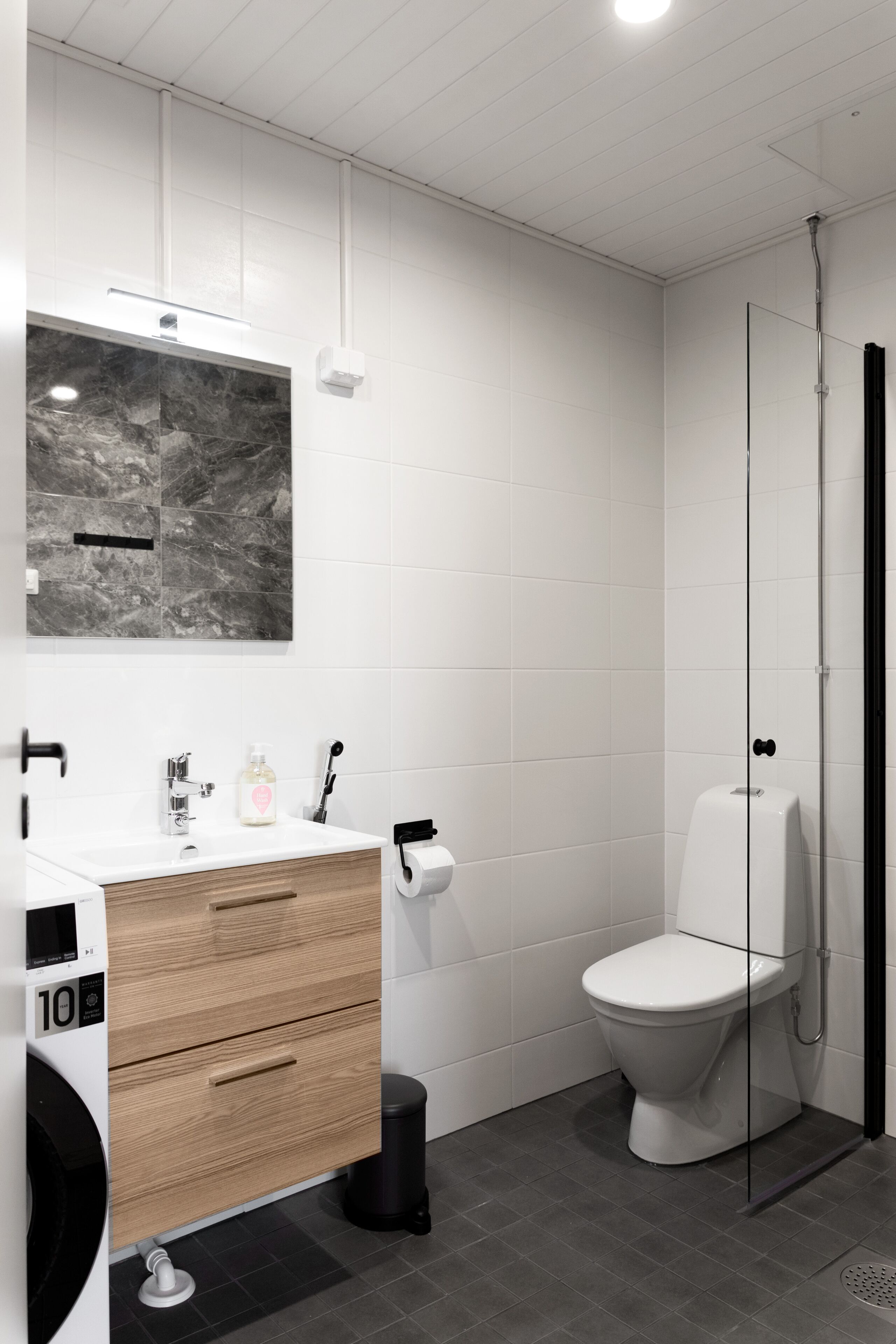 A modern bathroom with a white vanity, a marble backsplash, a toilet, and a glass shower enclosure.
