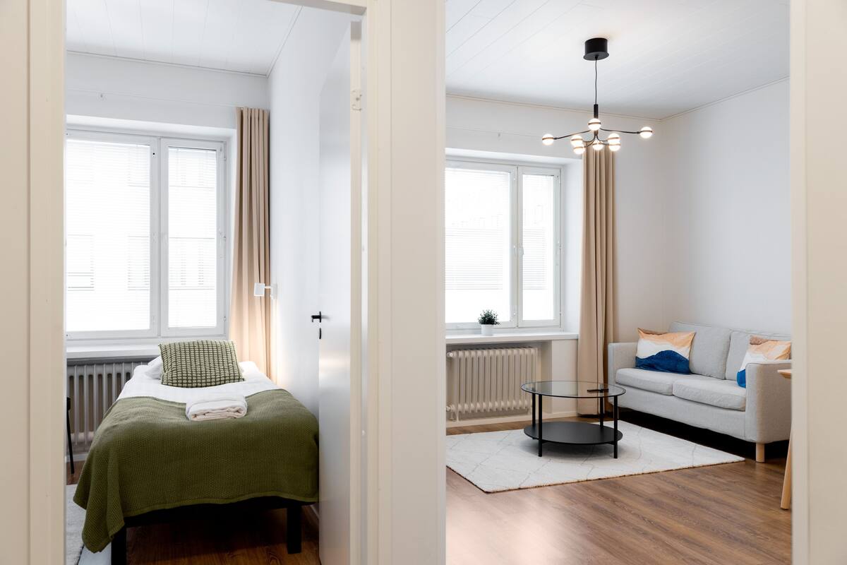 A modern room with a bed, a sofa, a small table, and a hanging light fixture.