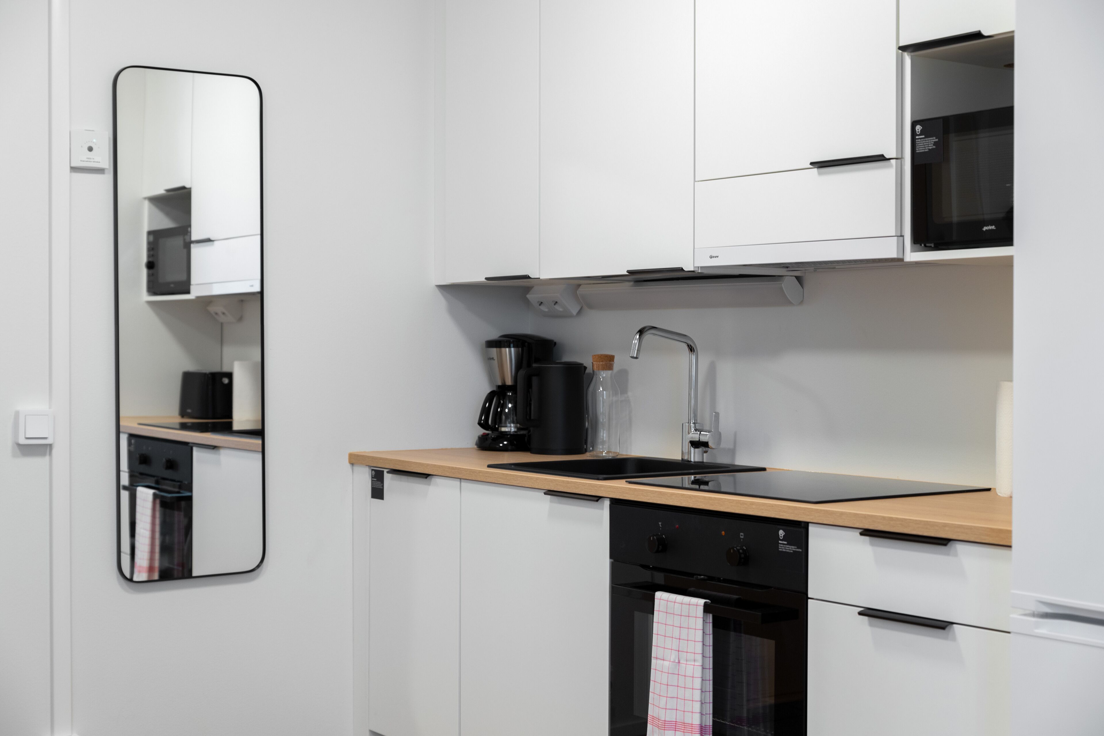 A modern kitchen with white cabinets, a wooden countertop, a black coffee maker, and a built-in oven.