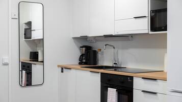 A modern kitchen with white cabinets, a wooden countertop, a black coffee maker, and a built-in oven.