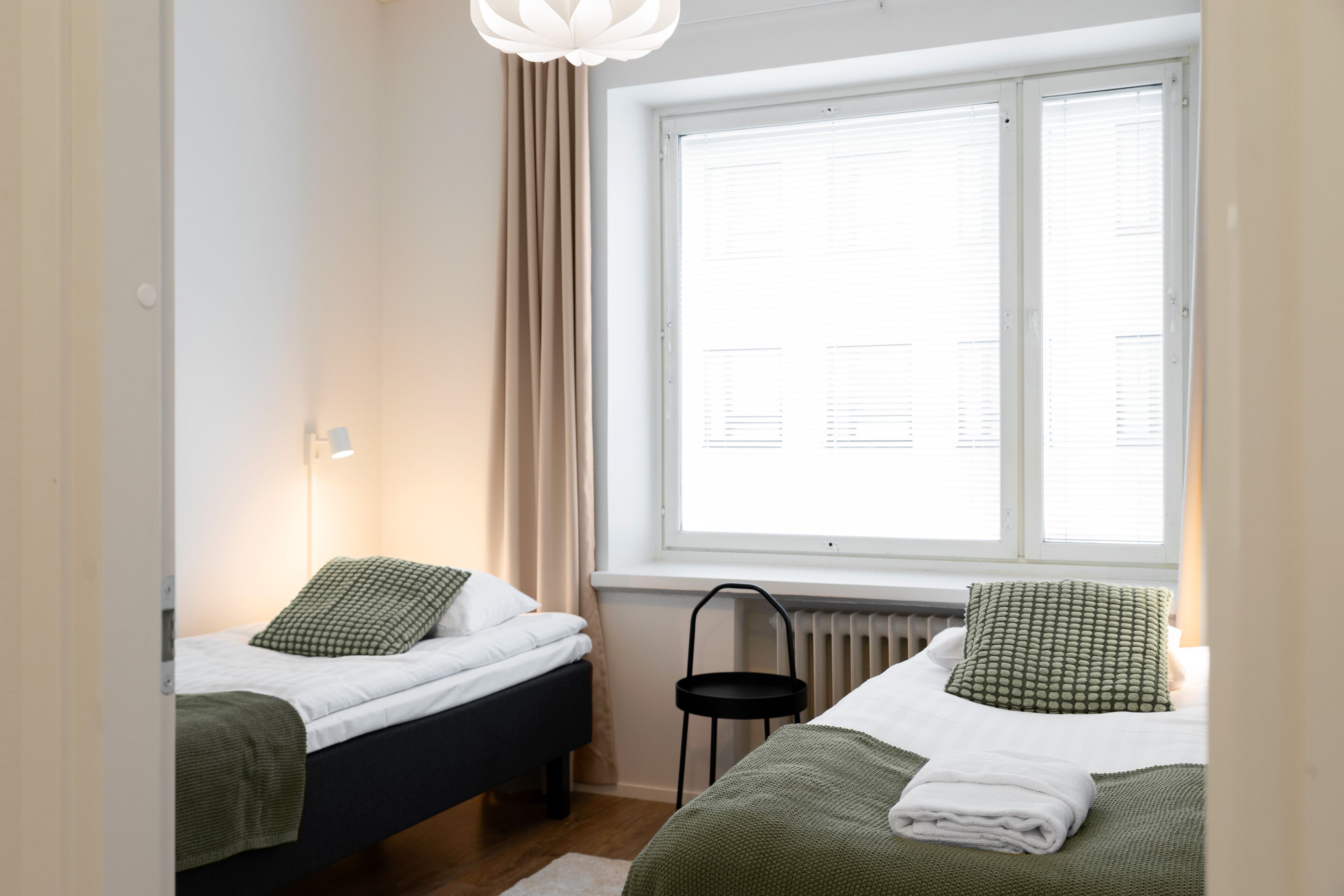 Une chambre avec deux lits, un radiateur et une fenêtre avec des stores.