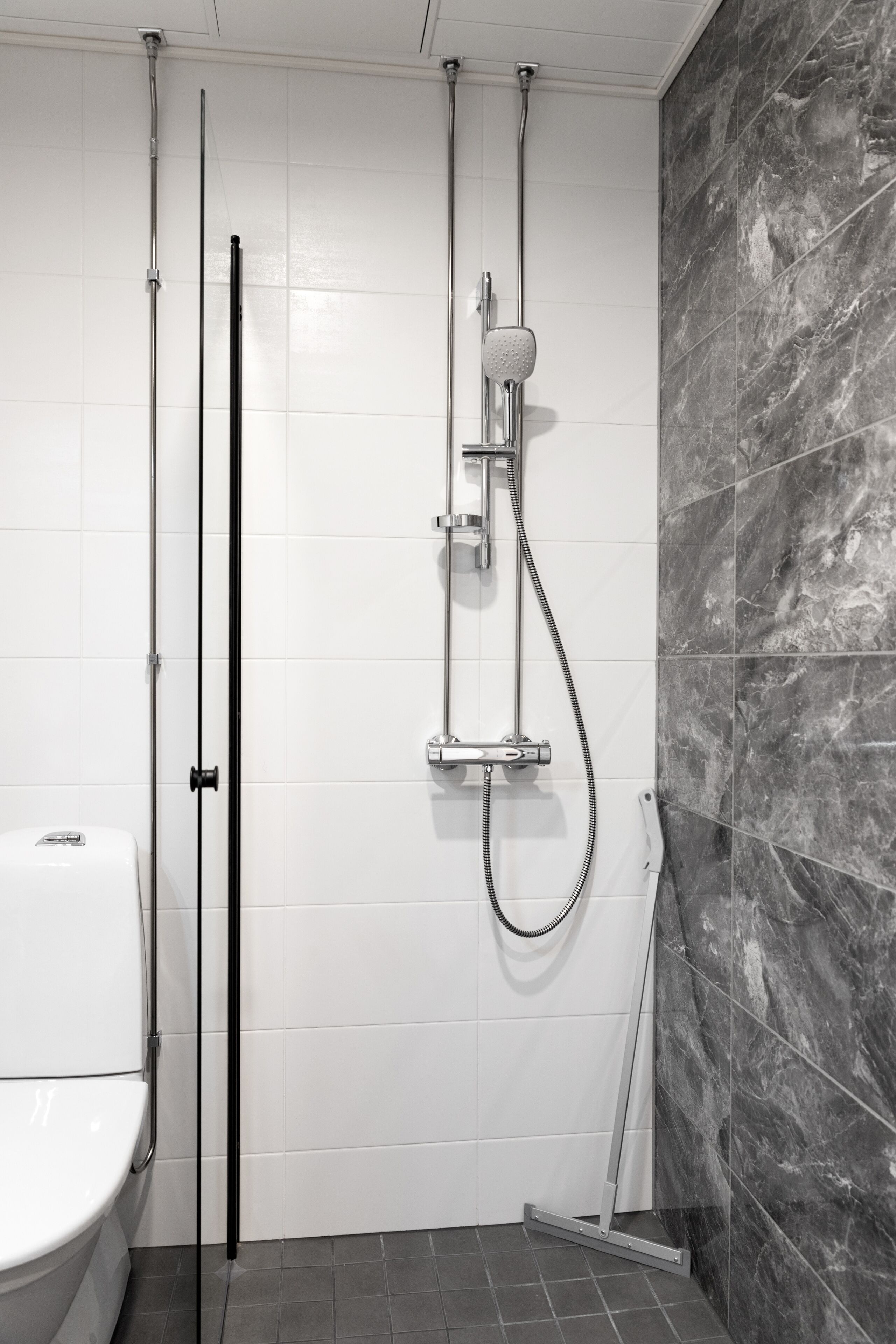 A modern bathroom with a shower, toilet, and a mop leaning against the wall.