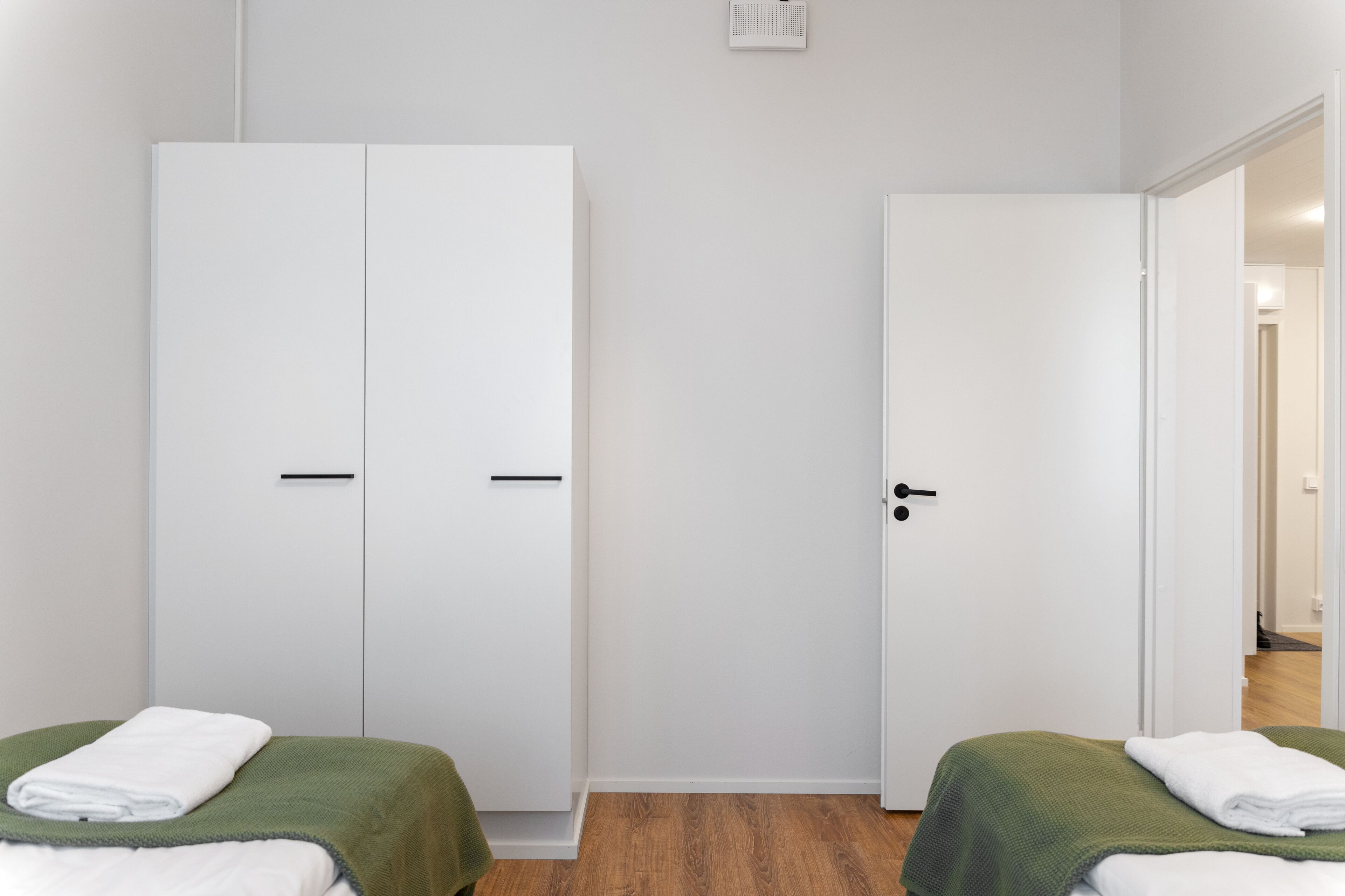 Ein Zimmer mit zwei Betten, jeweils mit grüner Decke und weißer Bettwäsche, sowie weißen Schränken mit schwarzen Griffen.