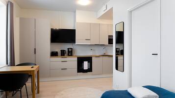 A compact hotel room with a kitchenette, a dining area, and a bed with a blue blanket.