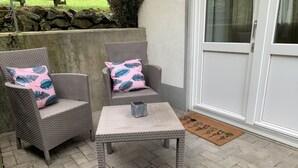 A patio area with two wicker chairs, each with a floral cushion, and a small table with a metal container. A doormat is visible at the entrance. - Moderne Ferienwohnung mit Eigener Terrasse (Arnsberg)
