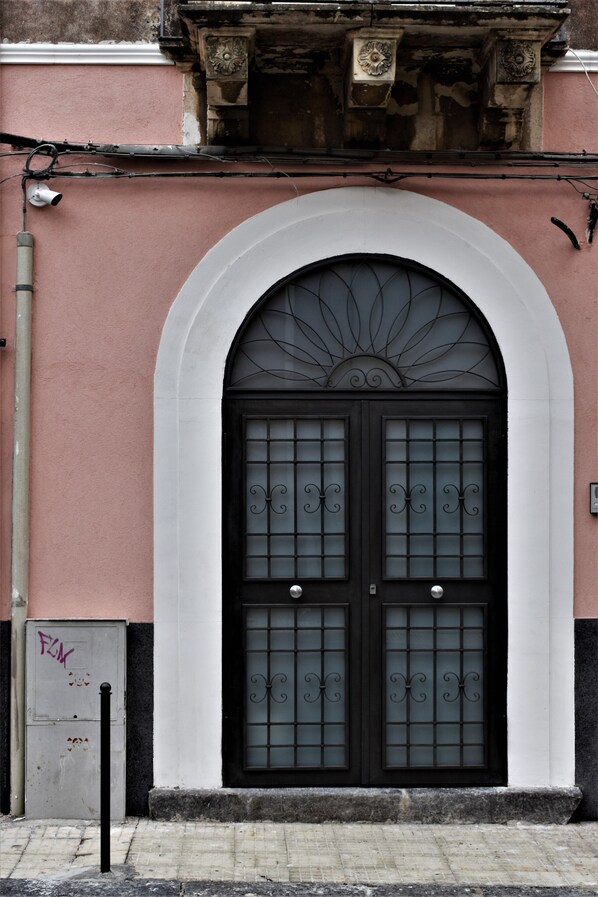 A black double door with decorative glass panels, set within a white arched frame on a pink building facade.