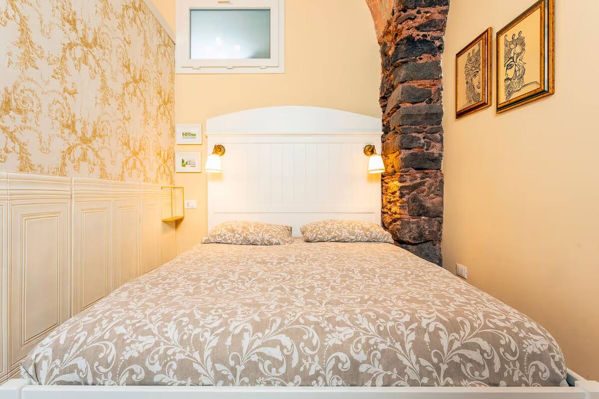 A bedroom with a bed, two bedside lamps, a TV, and a stone wall.