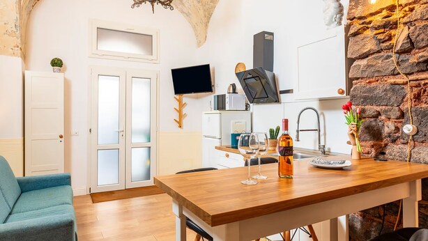 A modern kitchen with a stone accent wall, a dining area with a wooden table, and a blue sofa. - Casa Nirè - Casa Nirè II - Casa di Tano (Catania)
