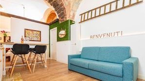 A modern living room with a blue sofa, wooden flooring, and a 'BENVENUTI' sign on the wall. - Casa Nirè - Casa Nirè II - Casa di Tano (Catania)
