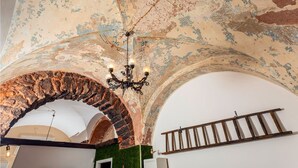 A room with a rustic ceiling, a stone archway, a chandelier, and a wooden ladder. - Casa Nirè - Casa Nirè II - Casa di Tano (Catania)