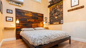 A bedroom with a wooden headboard, a bed with patterned bedding, two bedside lamps, and framed pictures on the walls. - Casa Nirè - Casa Nirè II - Casa di Tano (Catania)