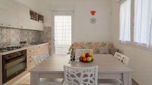A kitchen with a tiled backsplash, a stove, and a dining area with a table set for two. - 3768 Appartamento La Playa by Barbarhouse (Porto Cesareo)