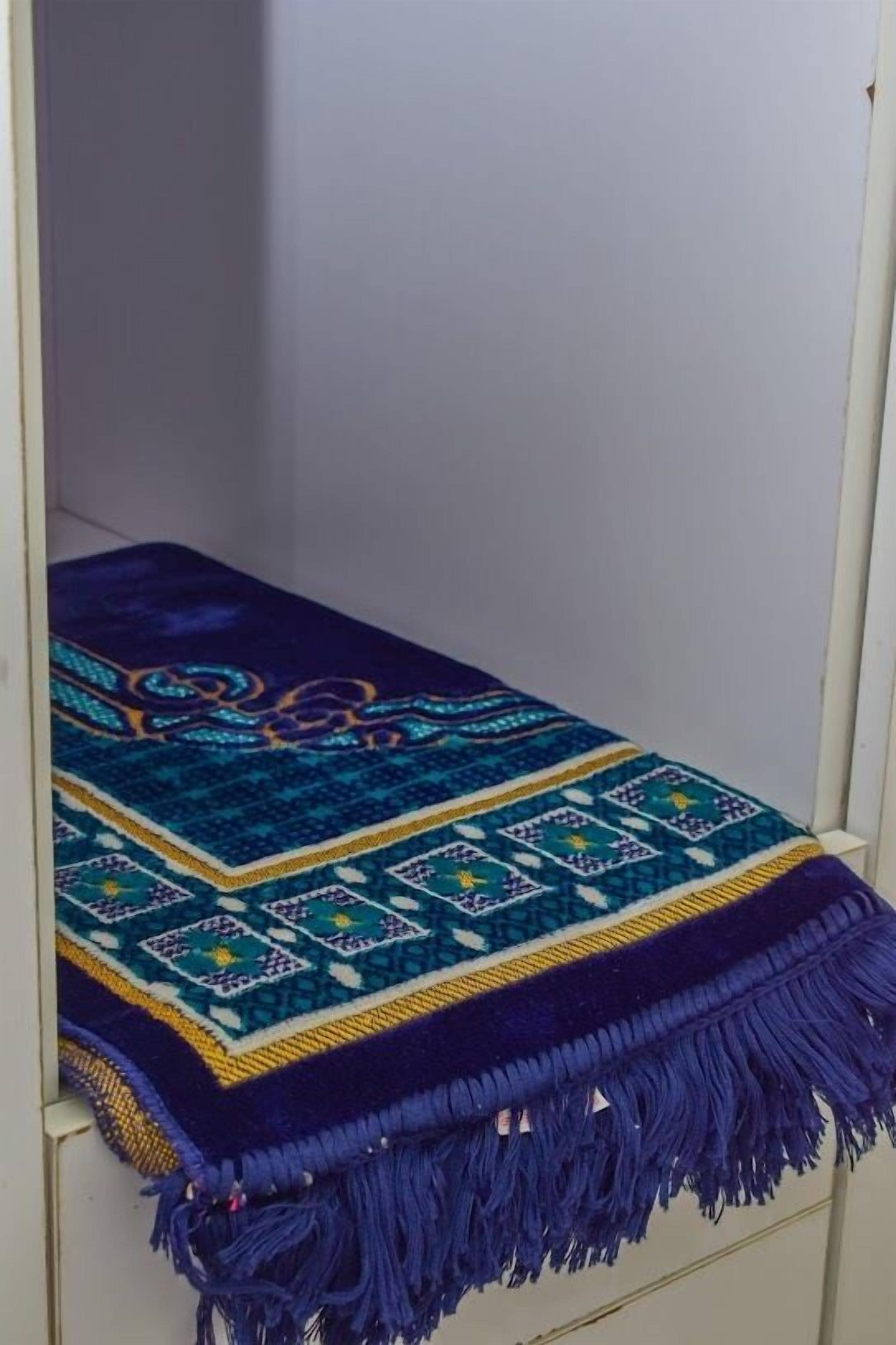 A bed with a blue and purple patterned blanket.