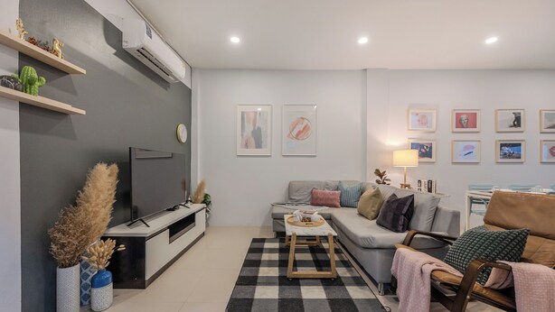 Ett modernt vardagsrum med en grå soffa, ett soffbord och en tv på ett svart tv-bord. Det finns dekorativa föremål på hyllor och en lampa på ett sidobord.