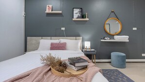 Ett modernt sovrum med en säng, sängbord, en spegel och en hylla med böcker och dekorativa föremål.