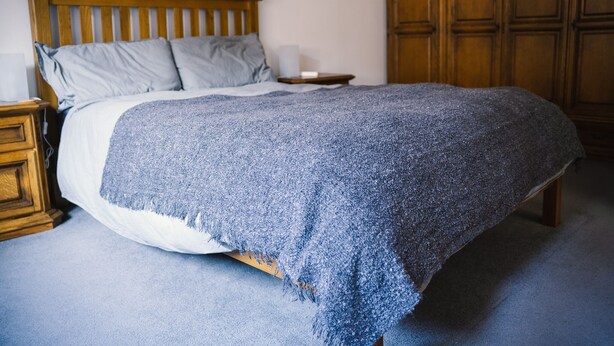 Une chambre avec un lit en bois, une table de chevet, une armoire en bois et une couverture bleue.