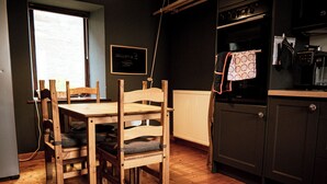 Une table de salle à manger en bois avec des chaises, un réfrigérateur noir et une fenêtre donnant sur l’extérieur.