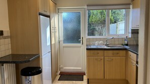 A compact kitchen with wooden cabinets, a built-in sink, and a window overlooking a garden. - Free Parking | Private Garden | Fully Equipped | Family Friendly | Bus Stop (Littlemore)
