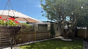 A backyard with a wooden deck, a hanging chair, a picnic table, and a garden area with a tree and flowers. - Free Parking | Private Garden | Fully Equipped | Family Friendly | Bus Stop (Littlemore)