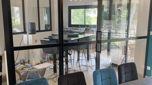 A modern dining area with a large table, blue chairs, and a view through glass walls to an outdoor balcony. - Villa Entre Pinède et Calanques de Marseille, 6 Chambres, 12 Couchages, Piscine (Marseille)