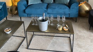 A living room with a blue sofa, a metallic coffee table with a champagne bottle and glasses, and a large tree mural on the wall. - Villa Entre Pinède et Calanques de Marseille, 6 Chambres, 12 Couchages, Piscine (Marseille)