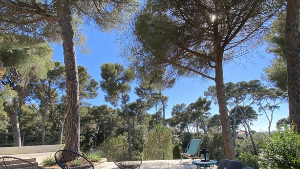 A wooden deck with outdoor furniture, including a sofa and chairs, surrounded by tall trees. - Villa Entre Pinède et Calanques de Marseille, 6 Chambres, 12 Couchages, Piscine (Marseille)