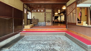 A traditional Japanese interior with tatami flooring, a wooden ceiling, and a red carpeted entrance.
