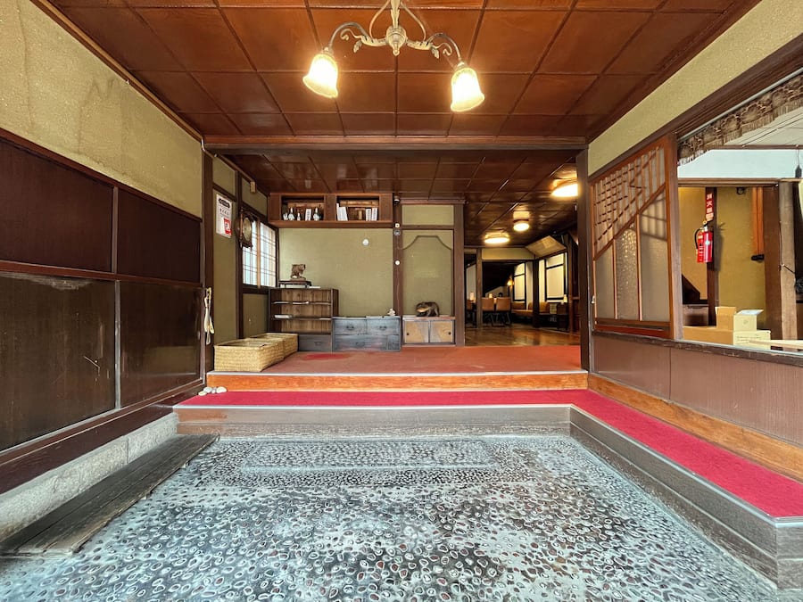 Ein traditionelles japanisches Interieur mit Tatami-Böden, einer Holzbalkendecke und einem roten Teppich als Eingangsbereich.