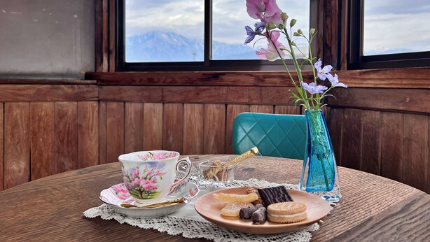 A wooden table with a floral teacup, a plate of cookies, and a vase with flowers.
