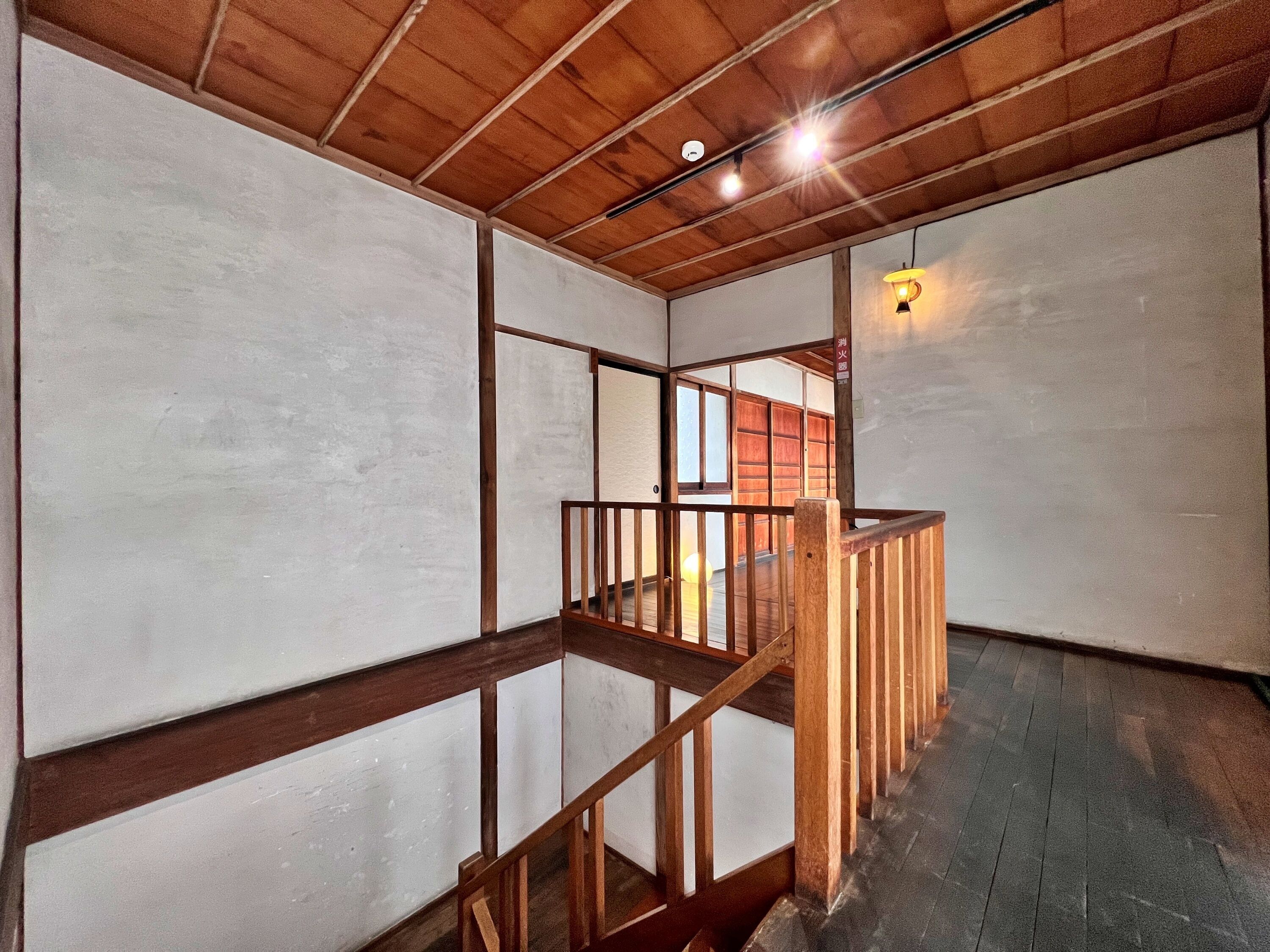 A room with a wooden ceiling, a wooden staircase, and a view of a traditional Japanese room with sliding doors.