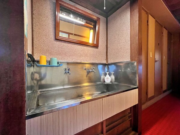 A bathroom with a stainless steel sink, a mirror above it, and a towel rack. - Matsubaya Guesthouse - Hostel (Omachi)