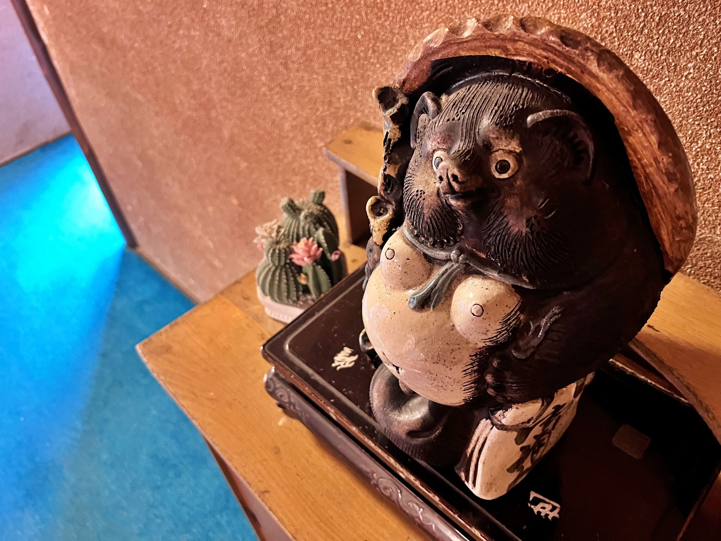Una mesa de madera con una figura de cerámica decorativa, un pequeño cactus y una zona iluminada en azul.