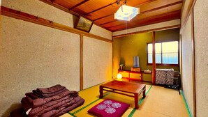 A traditional Japanese room with tatami flooring, a low wooden table, a cushion, and a hanging lantern.
