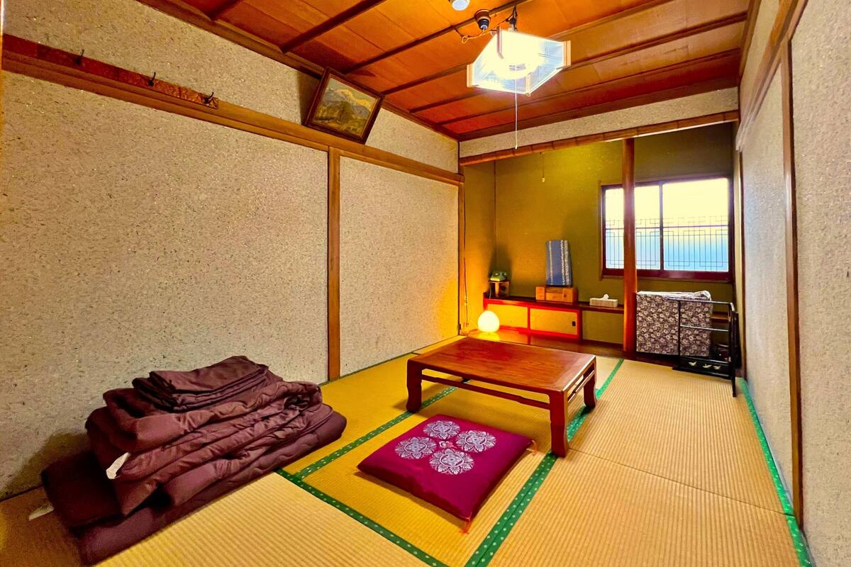Ein traditioneller japanischer Raum mit Tatami-Boden, einem niedrigen Holztisch, einem Kissen und einer hängenden Laterne.