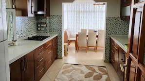 A kitchen with wooden cabinets, a tiled backsplash, a dining area with a table and chairs, and a ceiling light fixture. - Can Motel (Marmaris)