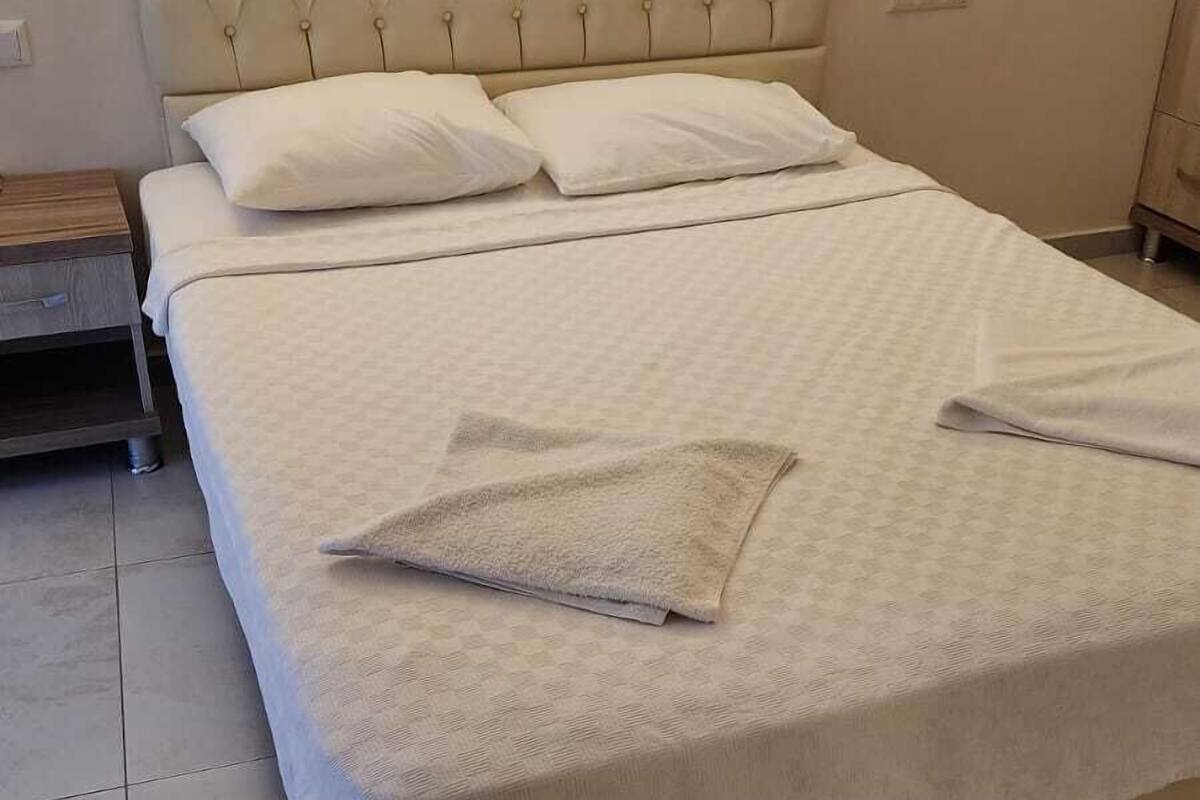 A neatly made bed with a tufted headboard, two bedside lamps, and a folded towel on the bed.