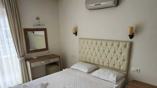 A neatly made bed with pillows and a folded towel, a bedside table, a nightstand, a mirror, and an air conditioning unit on the wall. - Can Motel (Marmaris)