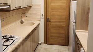 A compact kitchen with wooden cabinets, a sink, a stove, a refrigerator, and a washing machine. - Can Motel (Marmaris)