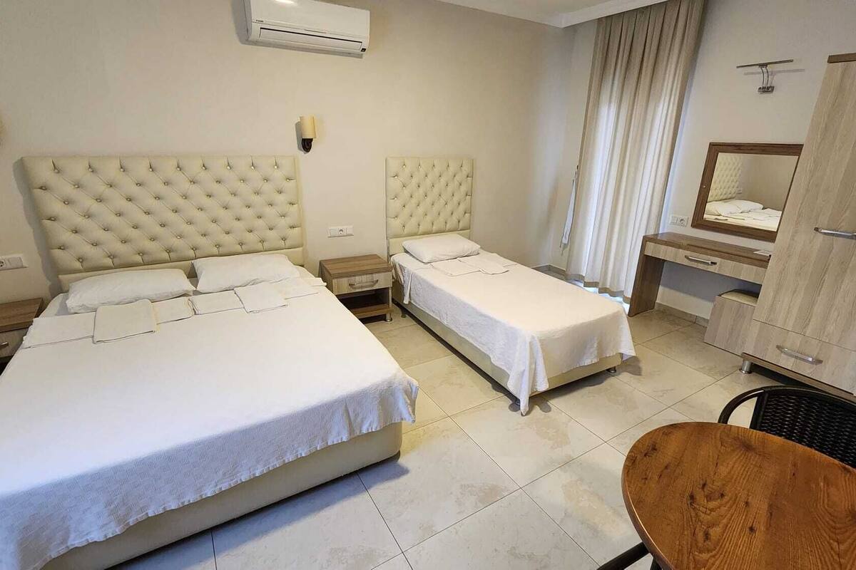 A hotel room with two beds, a wooden desk, a chair, a wardrobe, and a mirror.