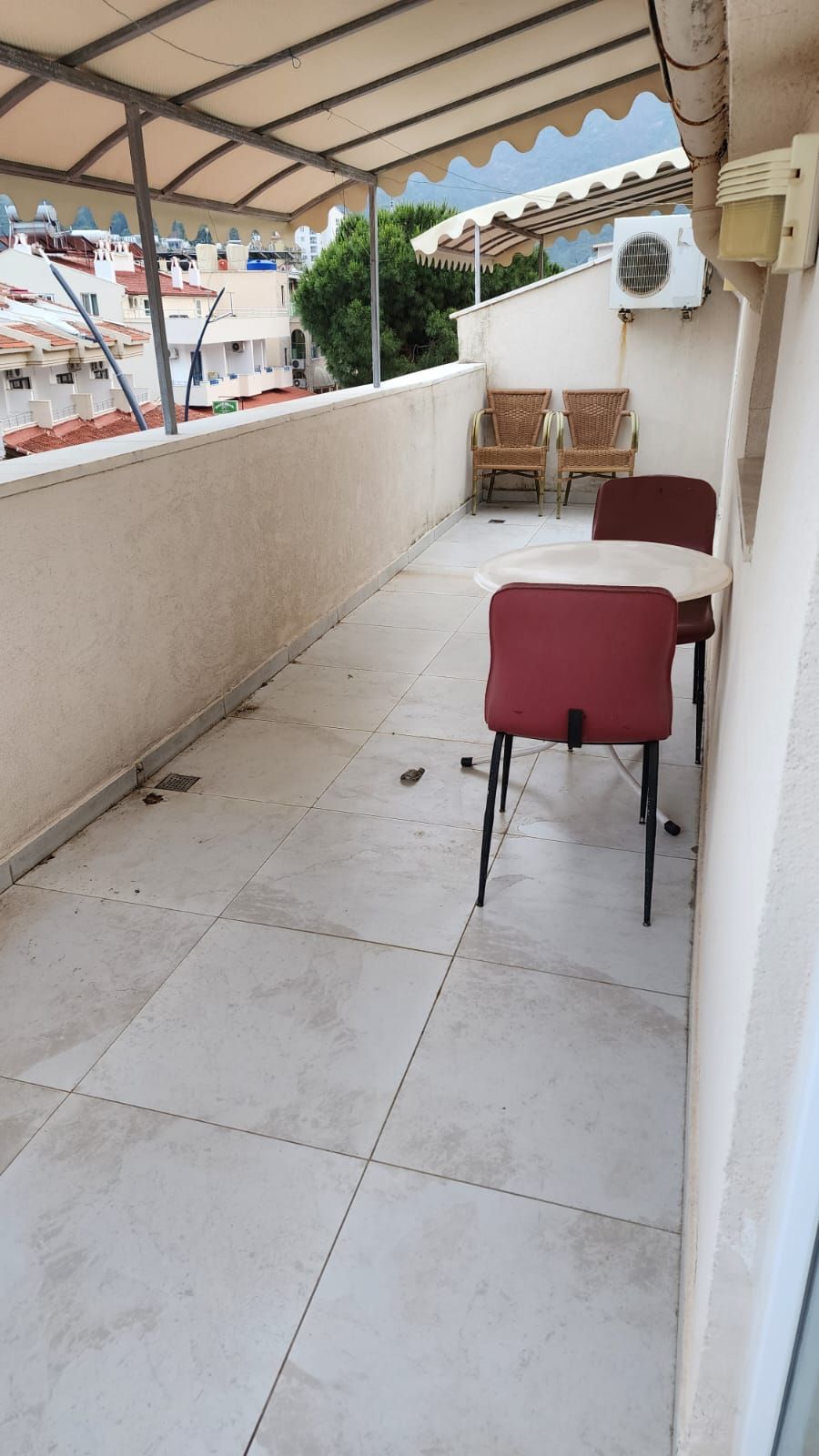 Un balcon extérieur couvert, doté d’un sol carrelé, de deux fauteuils en osier et d’une table.