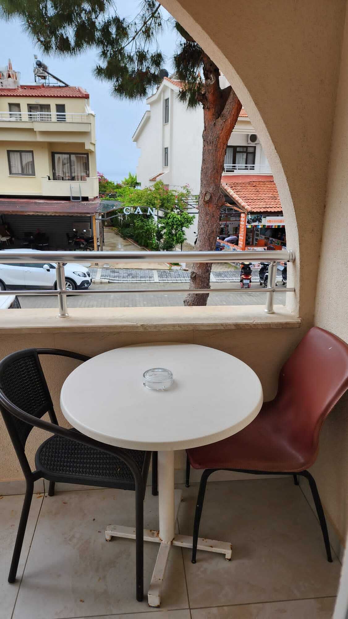 Un balcón con una mesa redonda y dos sillas, con vista a una calle con edificios y coches estacionados.