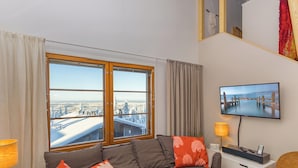 A modern living room with a large window, a flat-screen TV, and a sofa with decorative pillows.