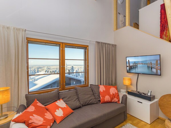 A modern living room with a large window, a flat-screen TV, and a sofa with decorative pillows.