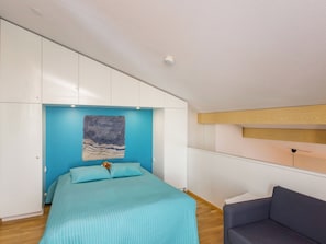 A bedroom with a bed, a blue wall, a wooden ceiling, and a grey sofa. - Kesä-iikka 4 by Interhome (Kuusamo)