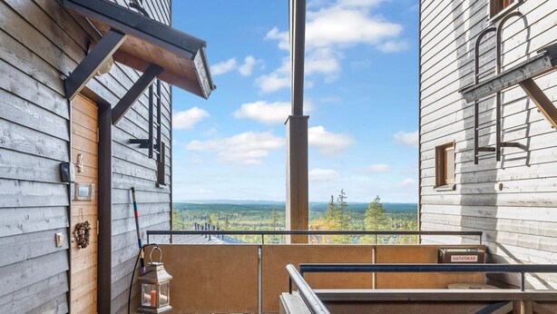 A wooden cabin with a balcony overlooking a forested landscape.