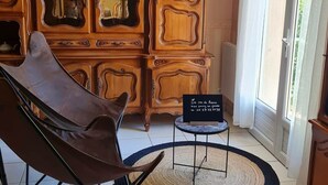 Un soggiorno moderno con una poltrona in pelle, un poggiapiedi rotondo intrecciato, un tavolino con un cartello e un mobile contenitore in legno con vetrate.