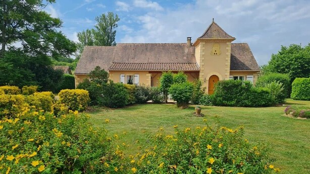 Un'ampia casa con tetto in tegole, circondata da giardini curati e cespugli fioriti di colore giallo.