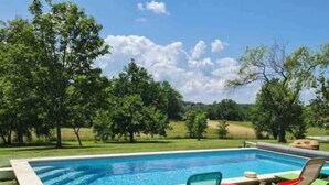 Una piscina rettangolare con bordo piastrellato, circondata da prato ben curato e alberi.